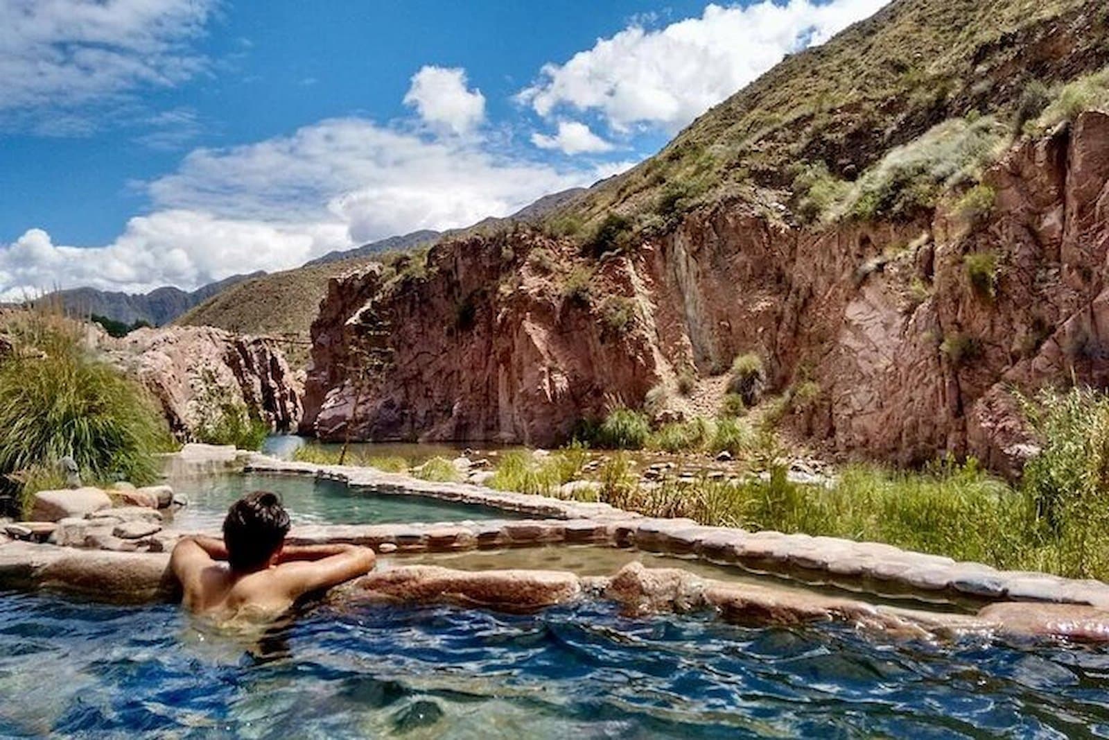 Man in a thermal pool with the Mendoza River canyon behind